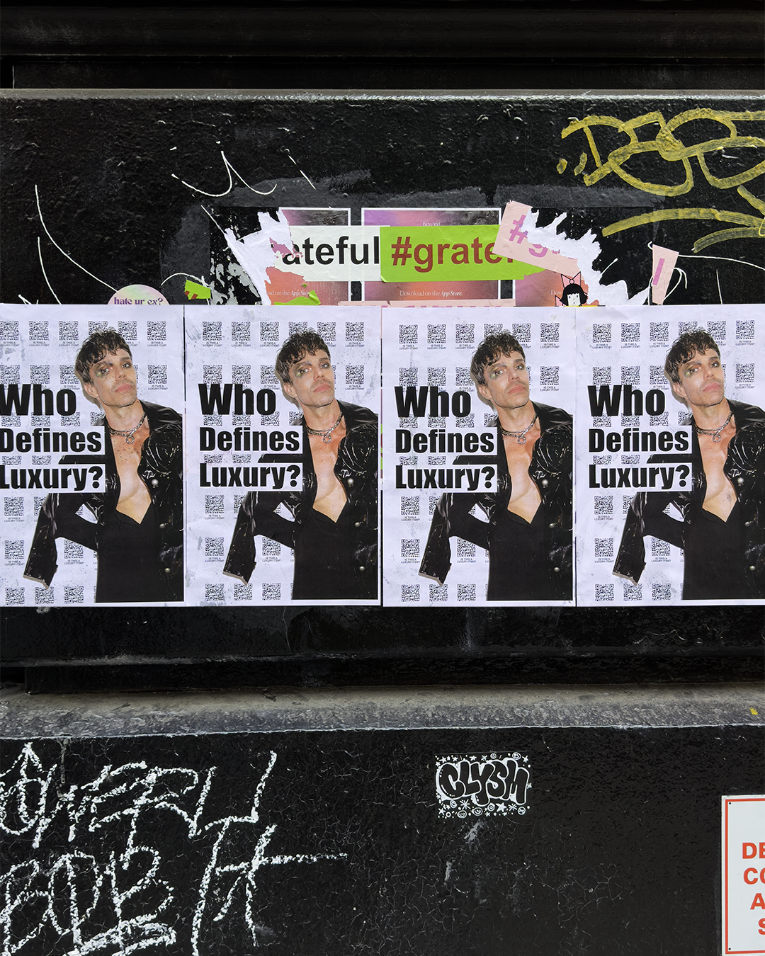 Four repeated Who Defines Luxury campaign posters featuring Patrick Duffy wheat-pasted on a black wall