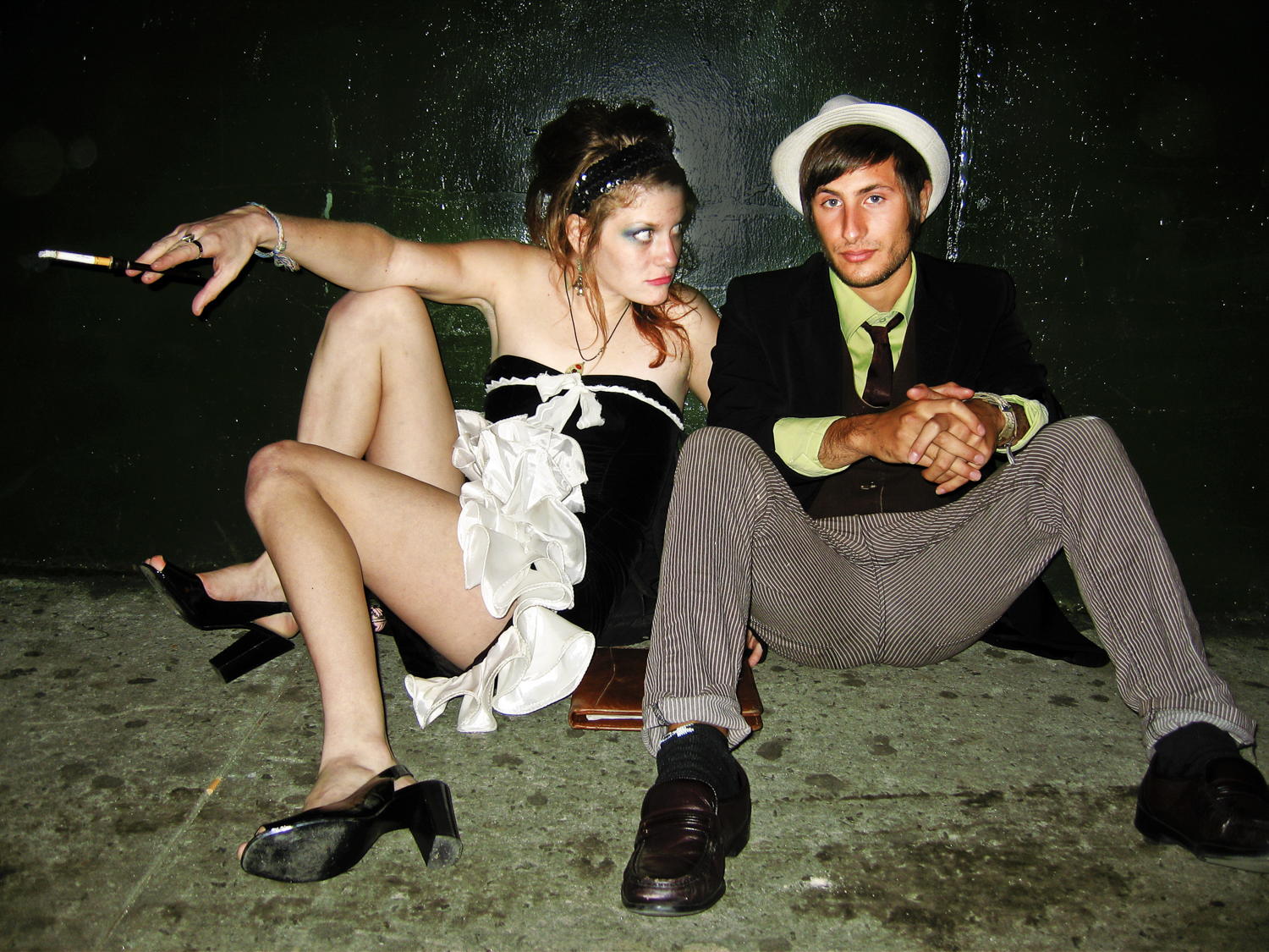 Two people seated against a dark green wall outside a New York club
