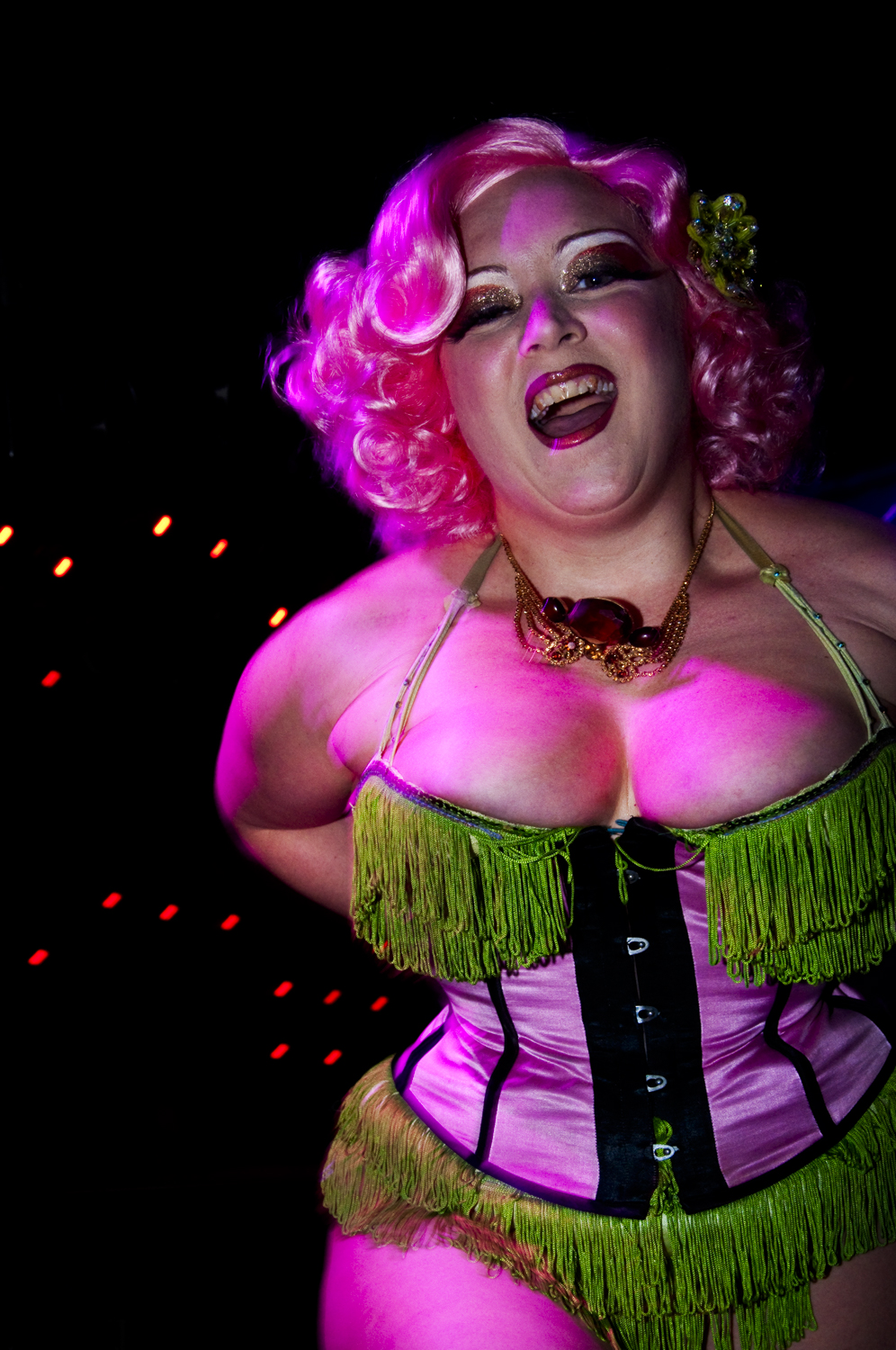 A pink-haired performer laughing beneath magenta club lights