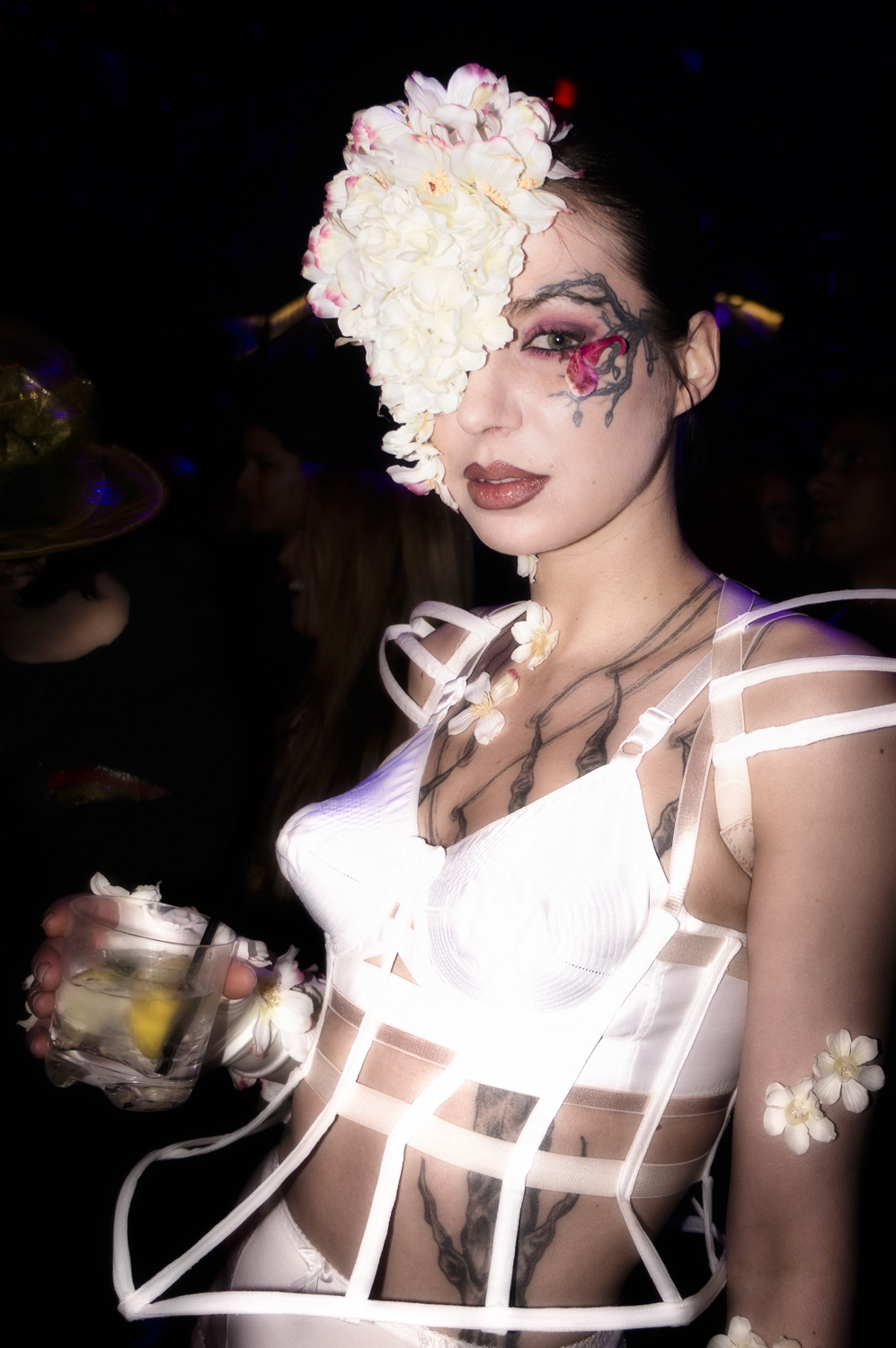 A nightlife portrait with white flowers, body drawing and a structured white outfit