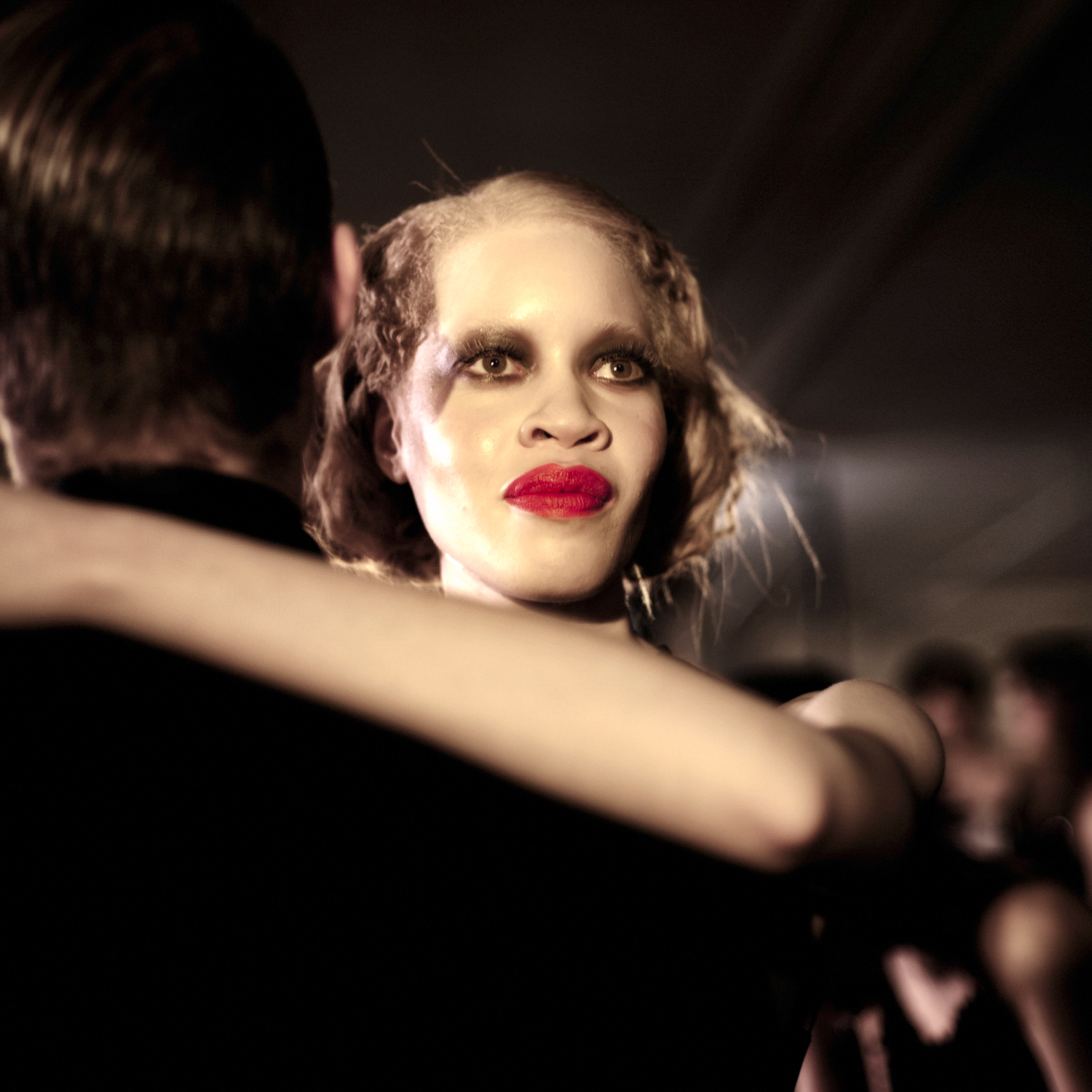 A softly lit club portrait with dramatic lashes and vivid red lipstick