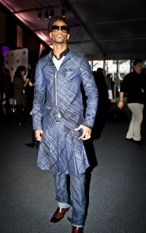 A man wearing an architectural blue jacket and skirt over cuffed jeans