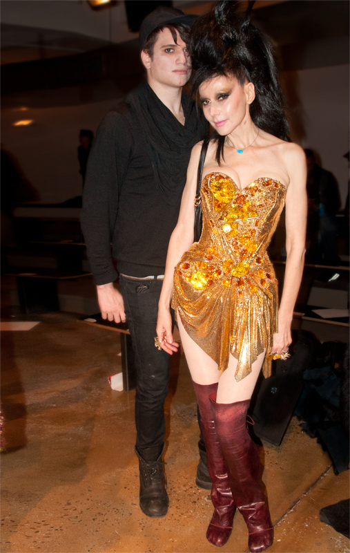 A woman in a sculptural gold dress and tall burgundy boots