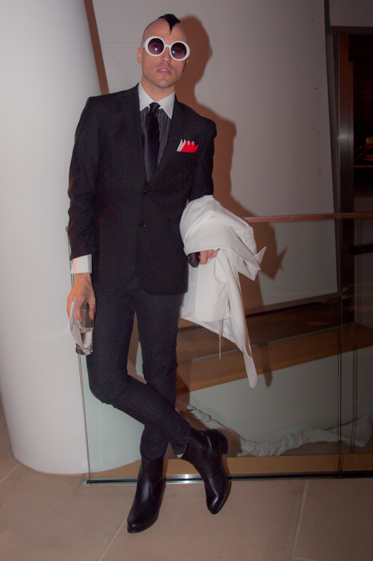 Tyler Glenn wearing a sharp black suit and white circular sunglasses