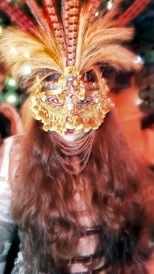 A nightlife portrait of a person wearing an elaborate orange feathered mask