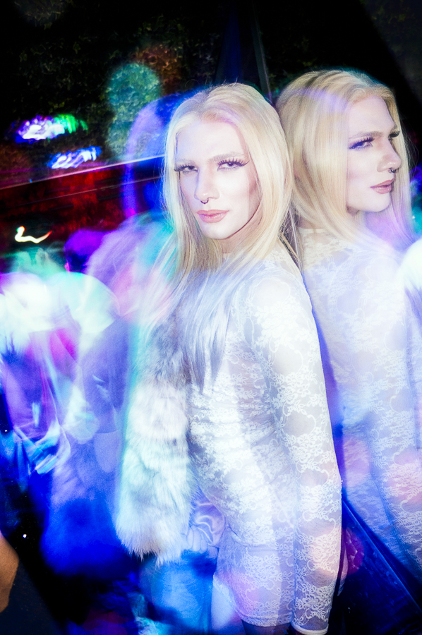 A blonde clubgoer in white lace doubled by a mirror and surrounded by colored light